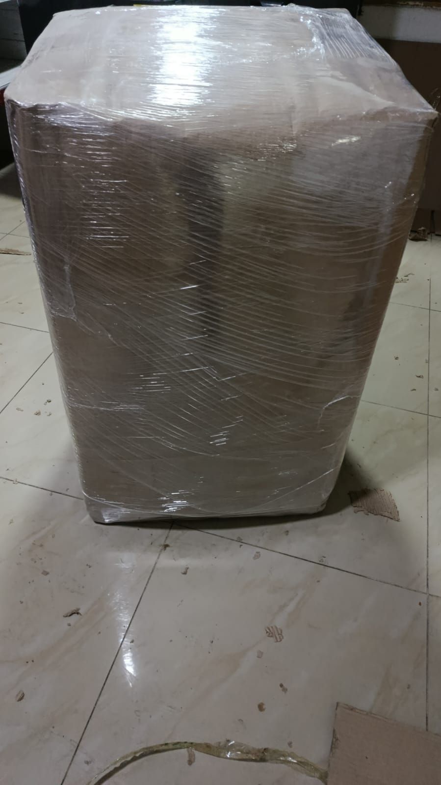 Caja de cartón envuelta en plástico sobre un suelo de baldosas.