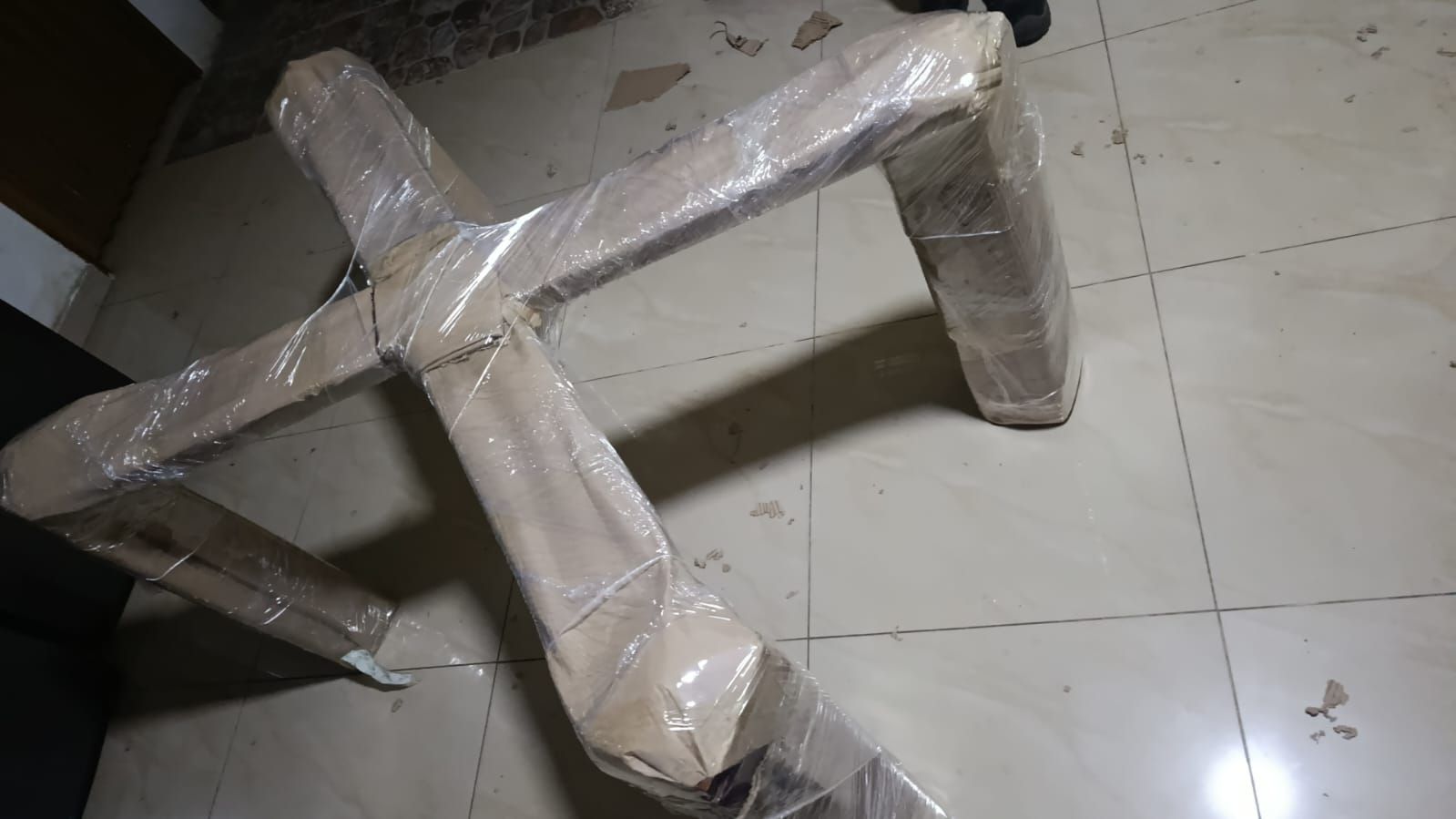 Estructura de mueble de cartón envuelta sobre un suelo de baldosas, con cinta adhesiva para asegurar las juntas.