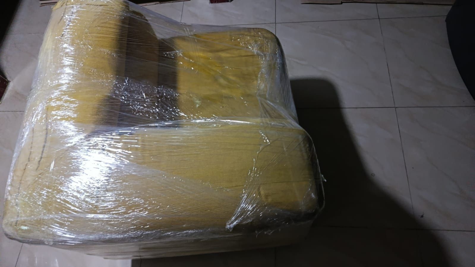 Sillón amarillo envuelto en plástico transparente sobre un suelo de baldosas en el interior.