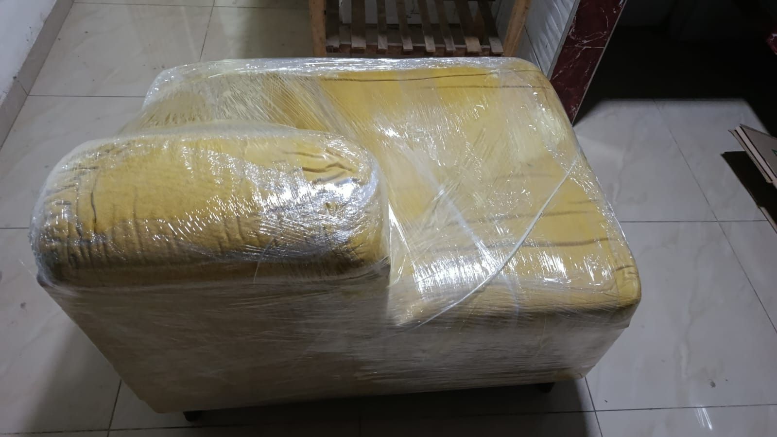 Sofá amarillo envuelto en plástico transparente sobre un suelo de baldosas.