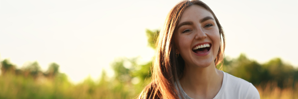 Smiling woman outdoors in a sunlit field with blurred greenery in the background