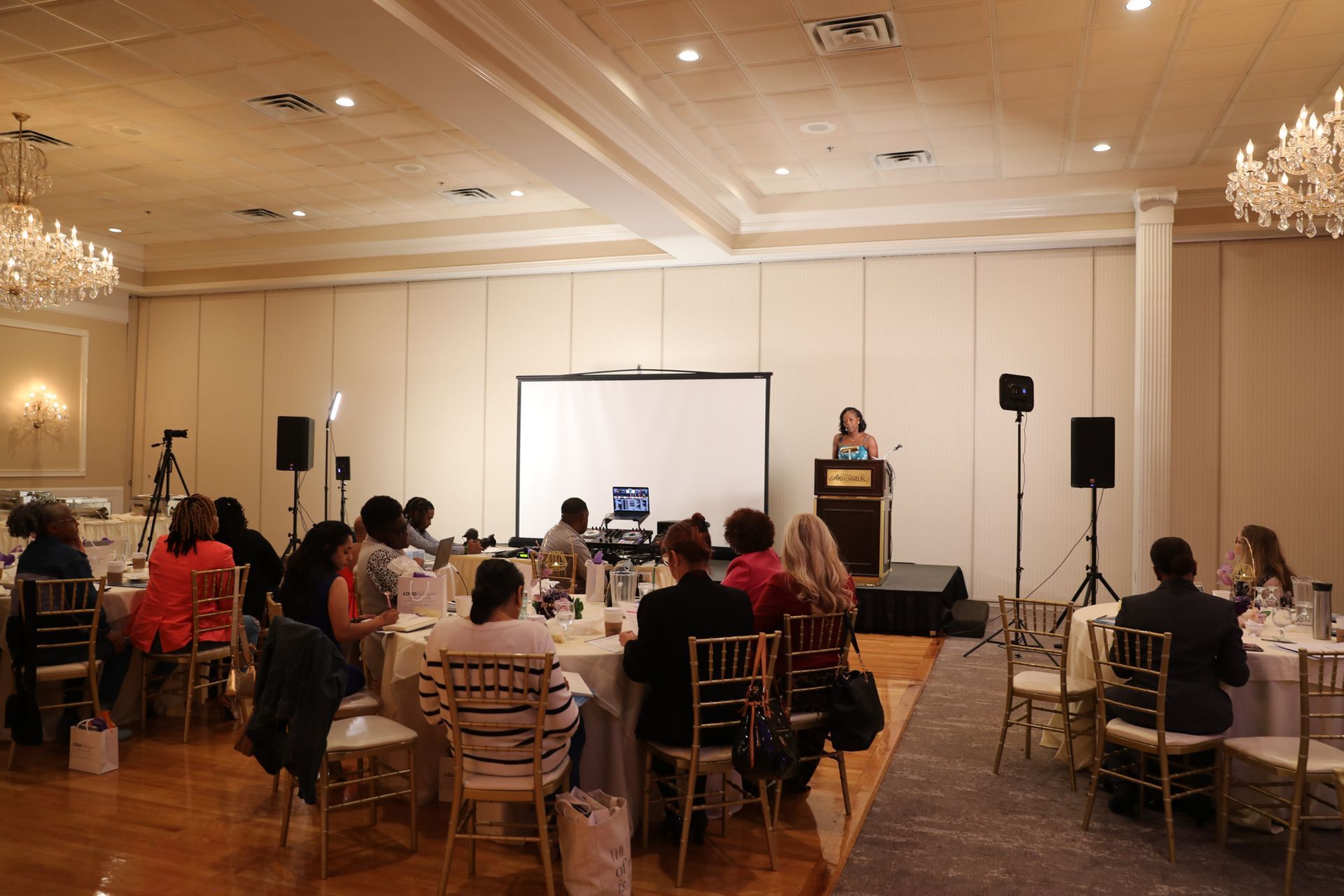 Conference room with seated audience facing a presentation screen and speaker at a podium