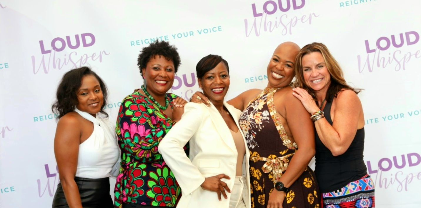 Four women posing and smiling at a Loud House event backdrop.