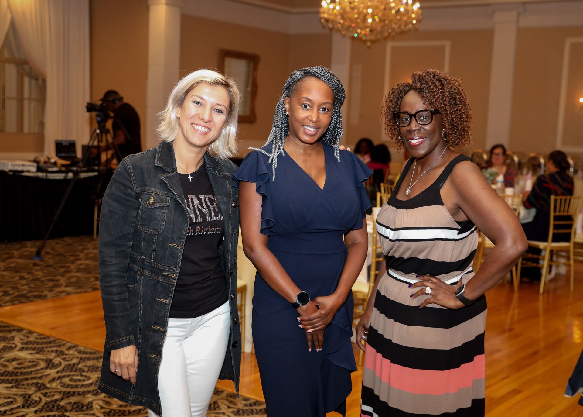 Three women smiling together in a room with a chandelier.