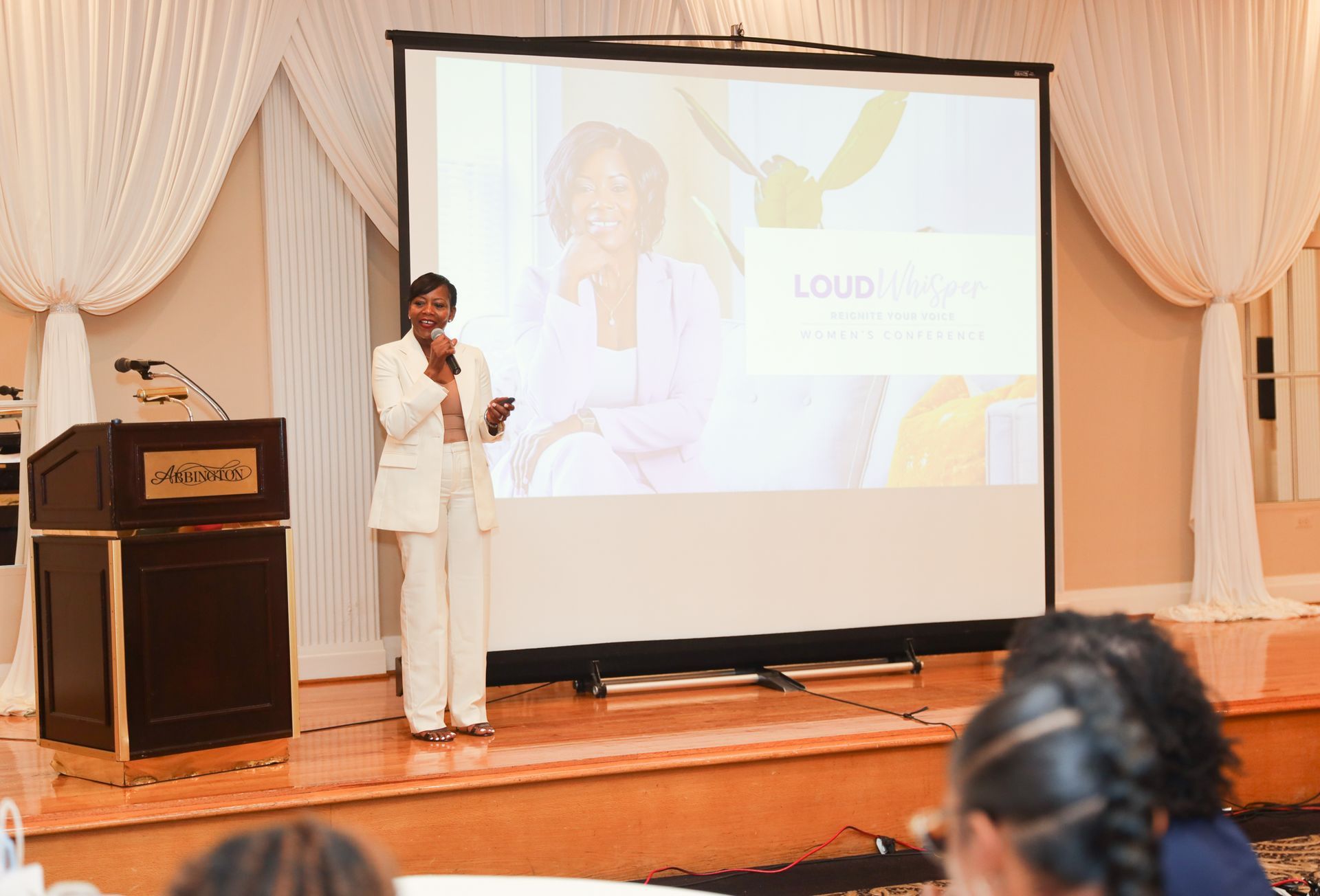 Woman giving a presentation on a stage, with a projector screen behind her.