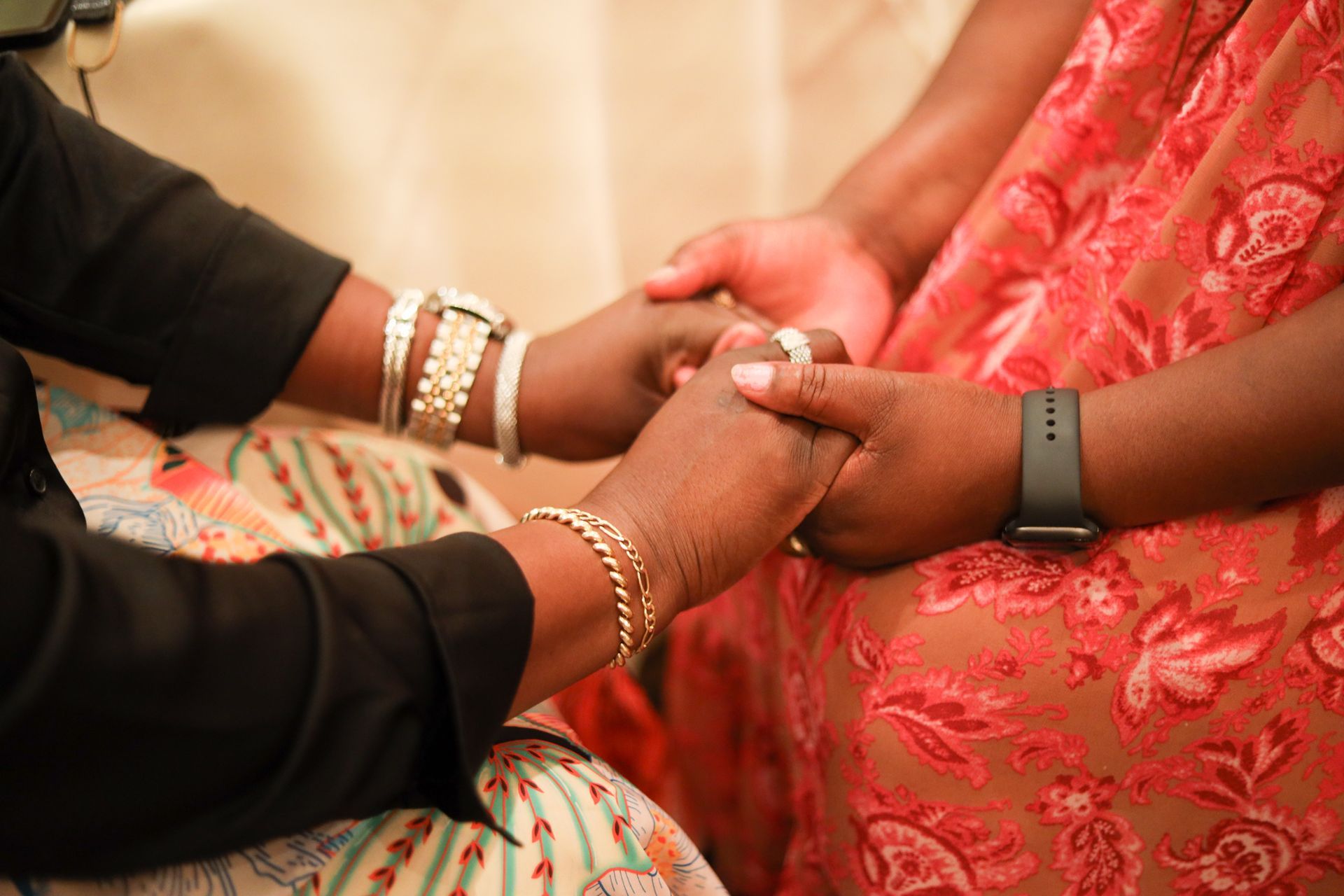 Two people holding hands; one wearing a black top and bracelets, the other in a red dress.