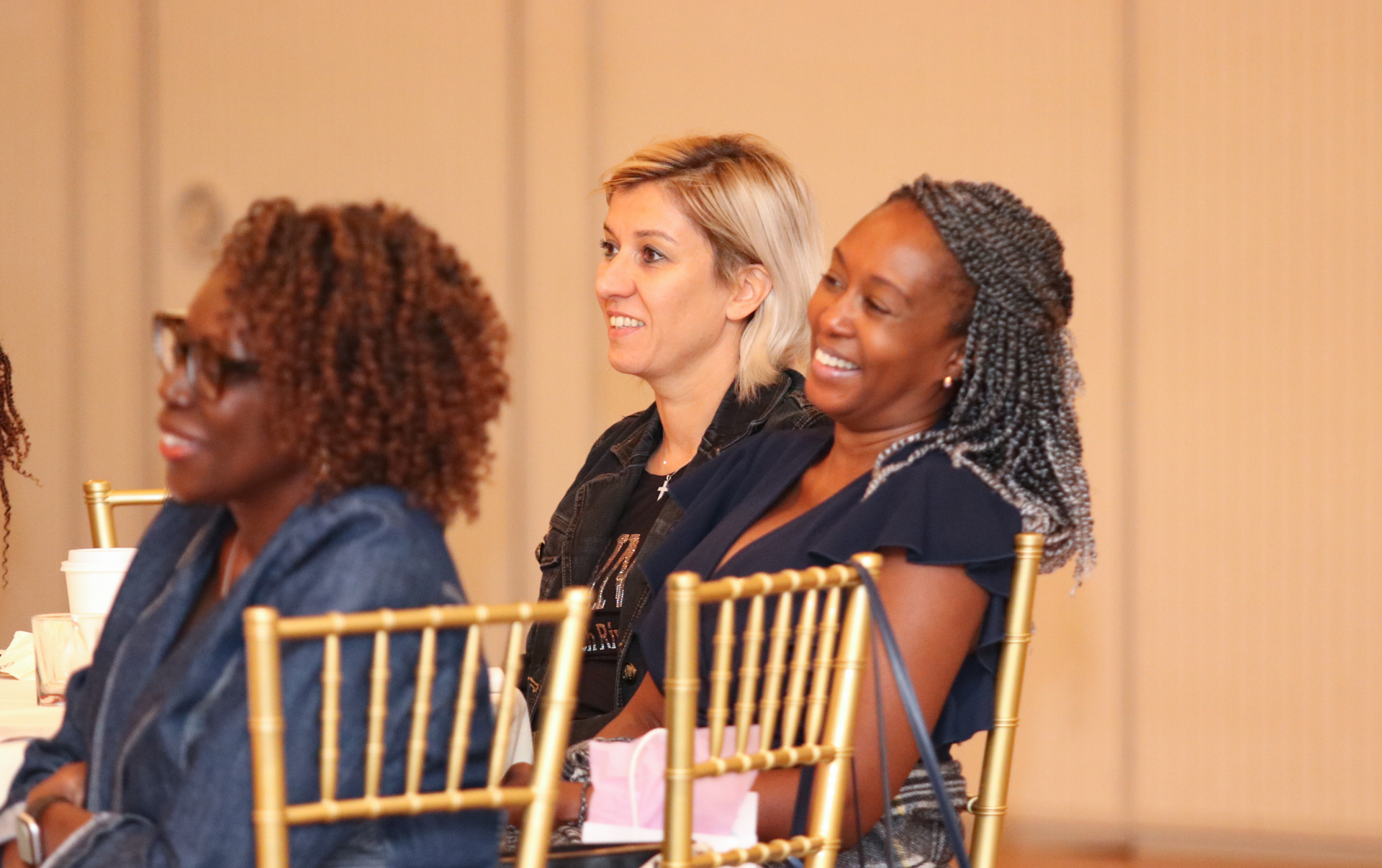 Three women seated, smiling, in a room with gold chairs.