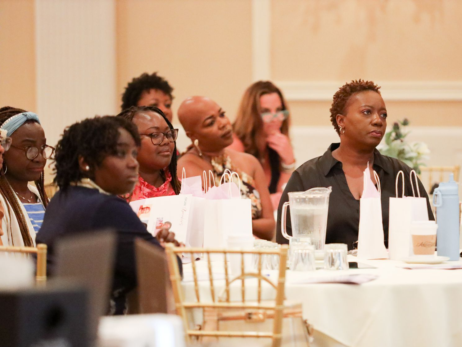 Audience seated at a banquet table, listening attentively in a formal event hall.