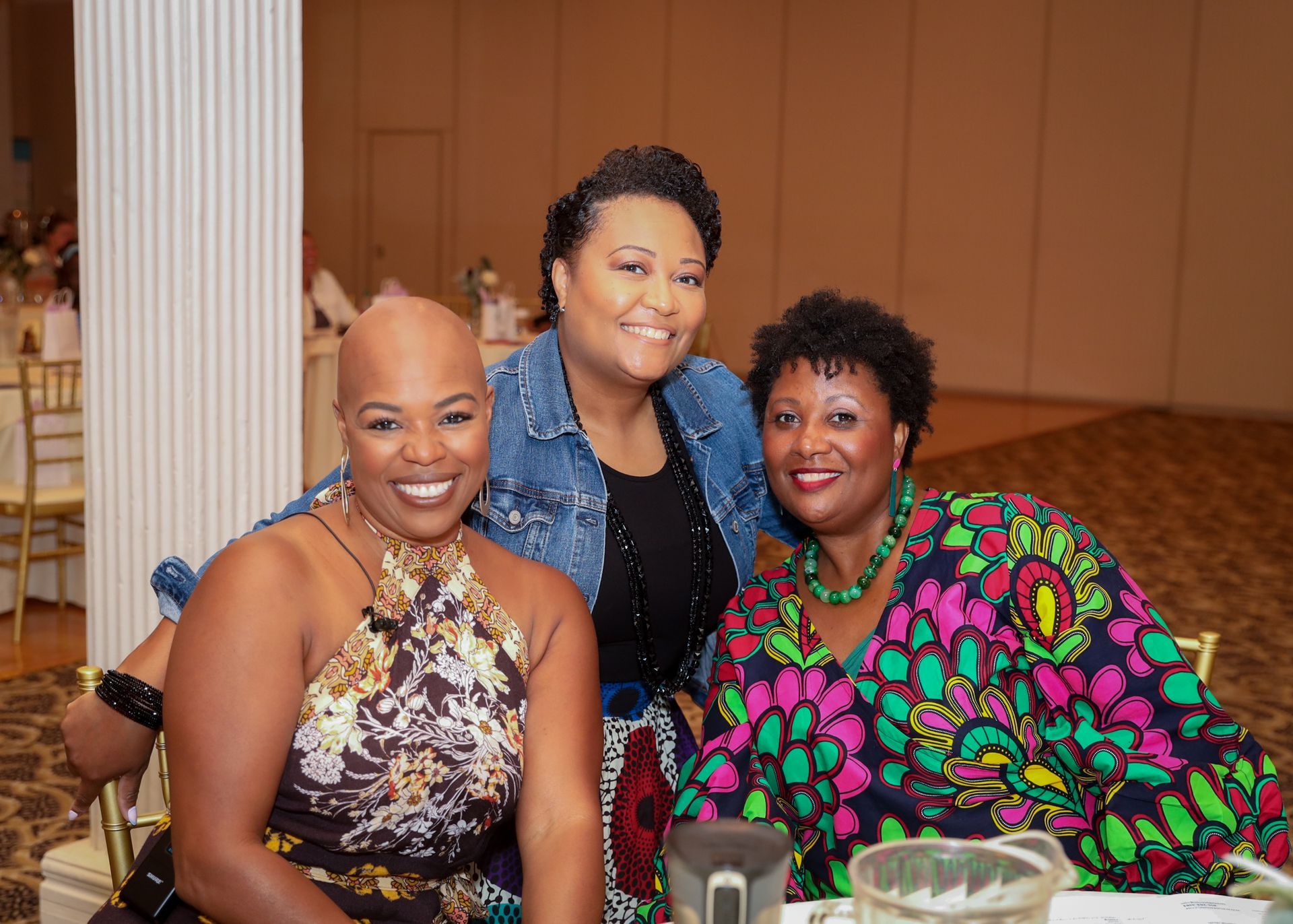 Three women smiling together at a formal event, one in a colorful print dress.