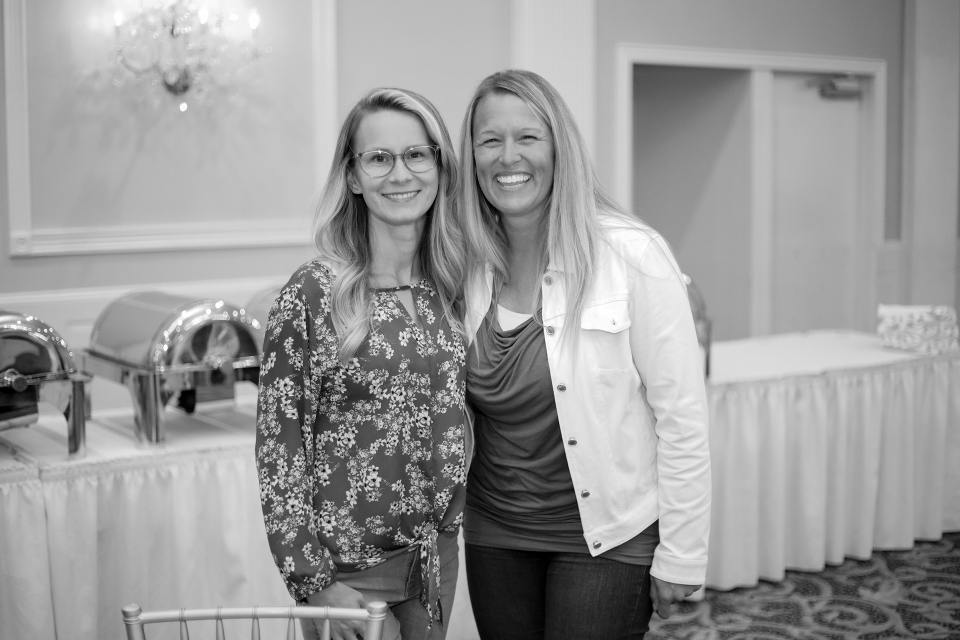 Two women smiling together, posing in front of a buffet table at an event.