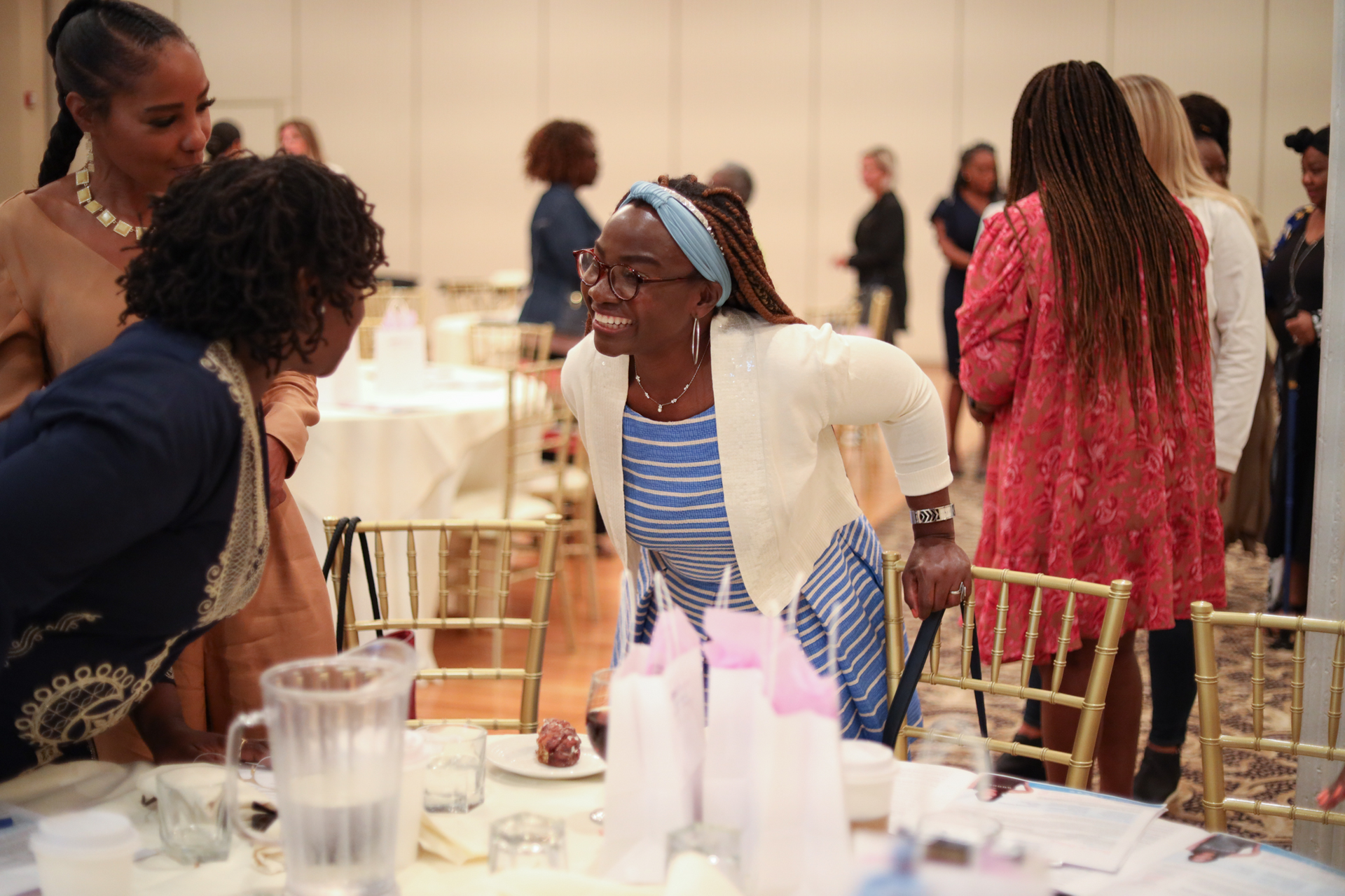 Two women conversing at a banquet table; one gestures emphatically. Others in background.