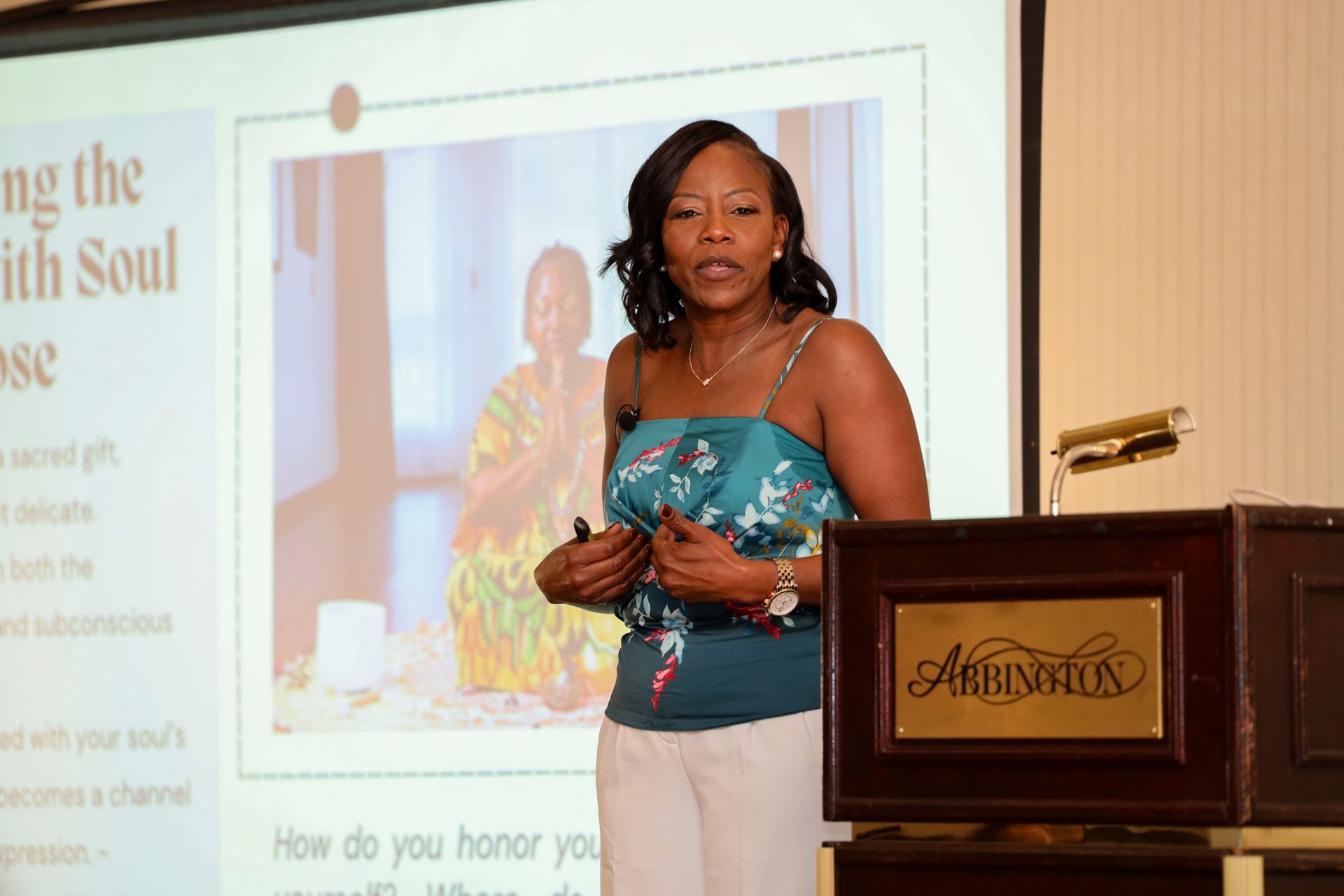 Woman speaking at a podium during a presentation, with a projected slide behind her.