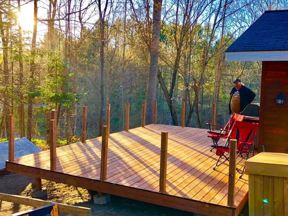 A man is standing on a wooden deck in the woods.