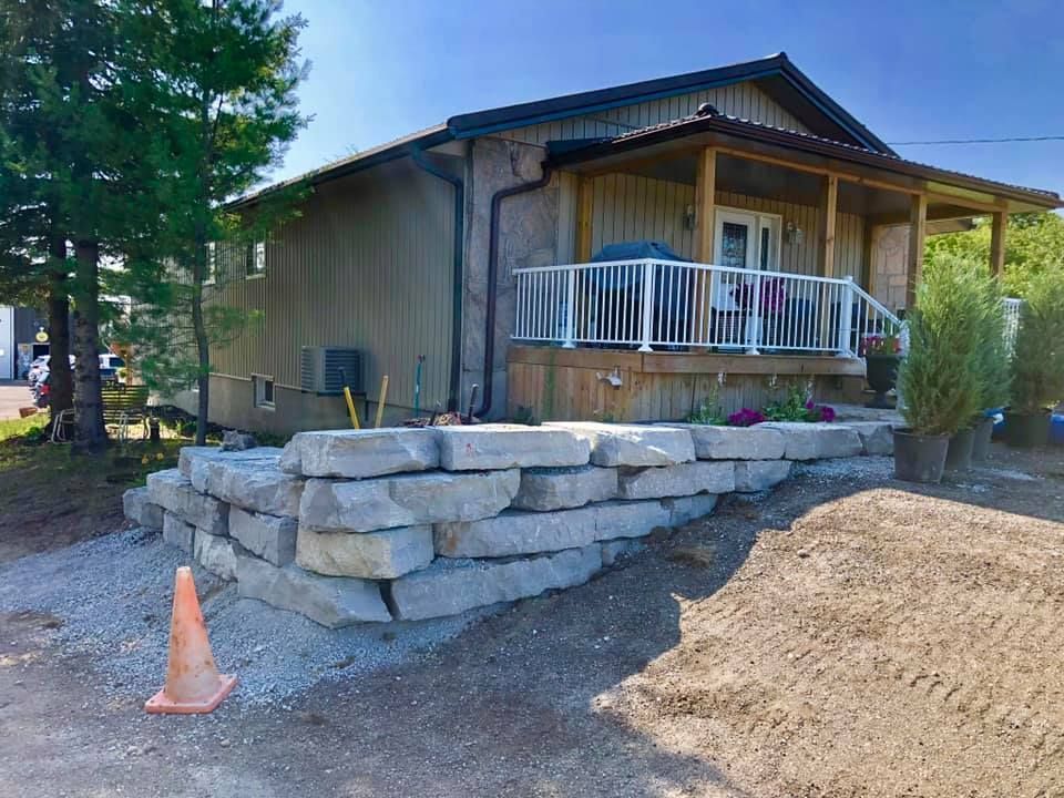 A house with a porch and a stone wall in front of it.
