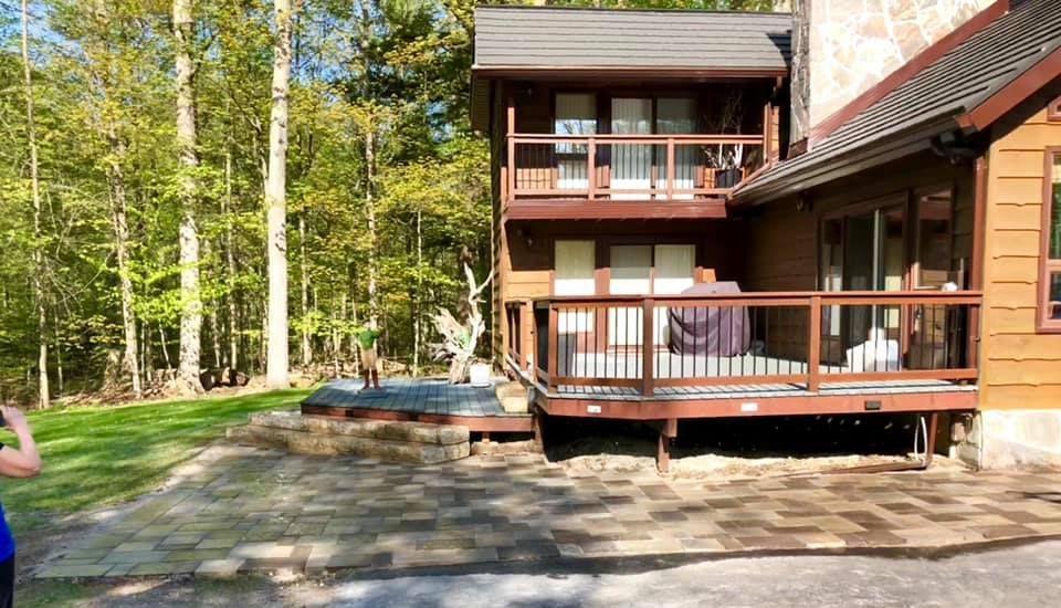 A man is standing in front of a house with a large deck.