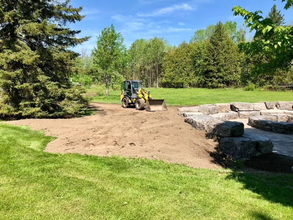 A bulldozer is moving dirt in a yard with trees in the background.