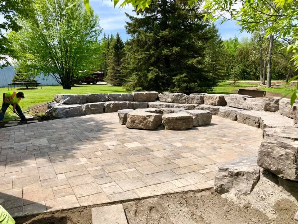 A man is working on a patio with a fire pit in the middle of it.
