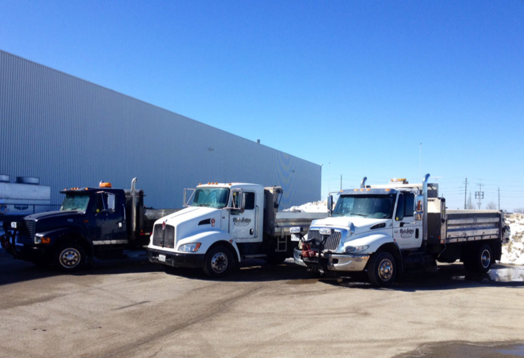 Three trucks are parked in a parking lot in front of a building.