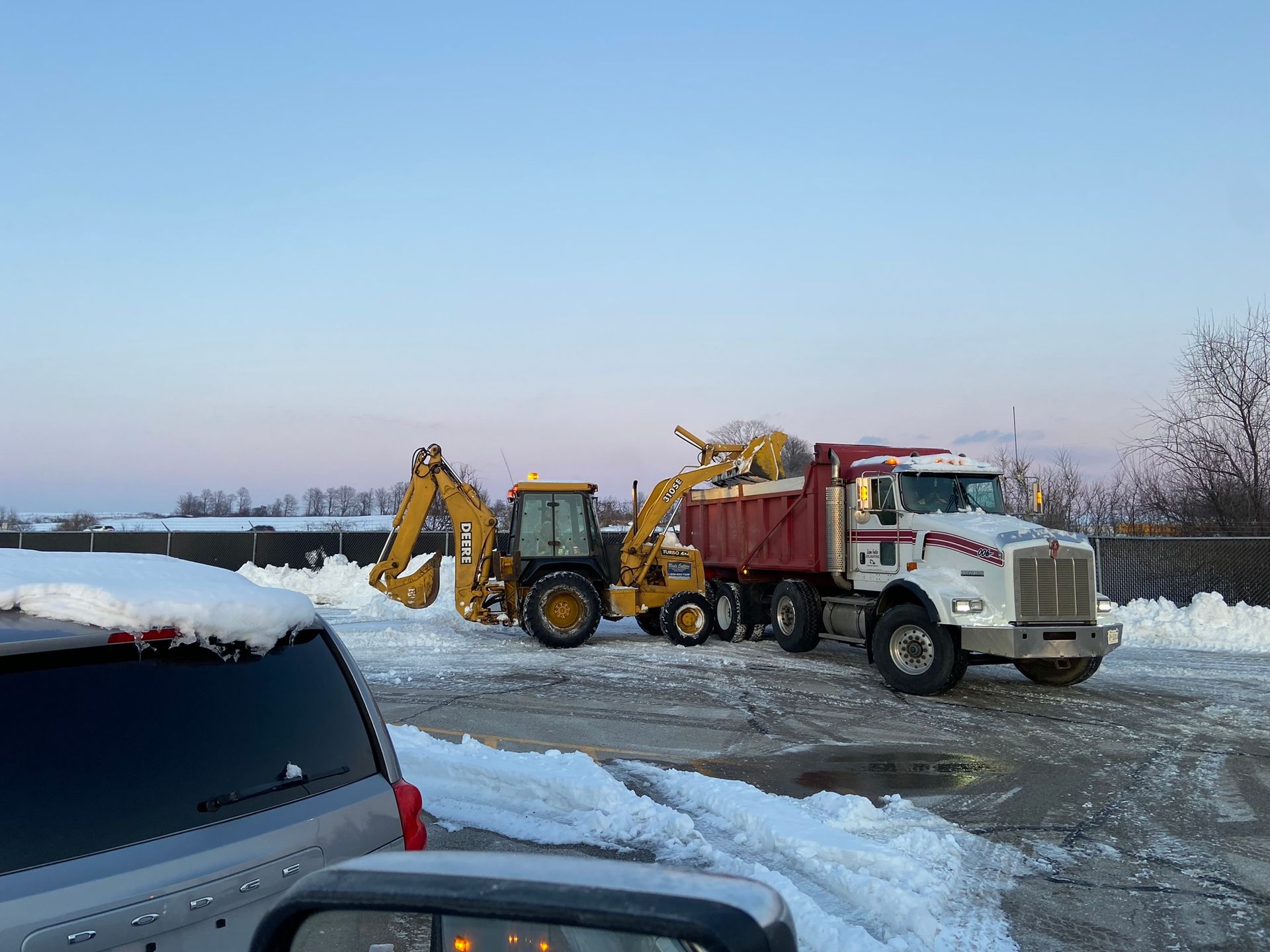 A dump truck is parked next to a tractor in the snow.