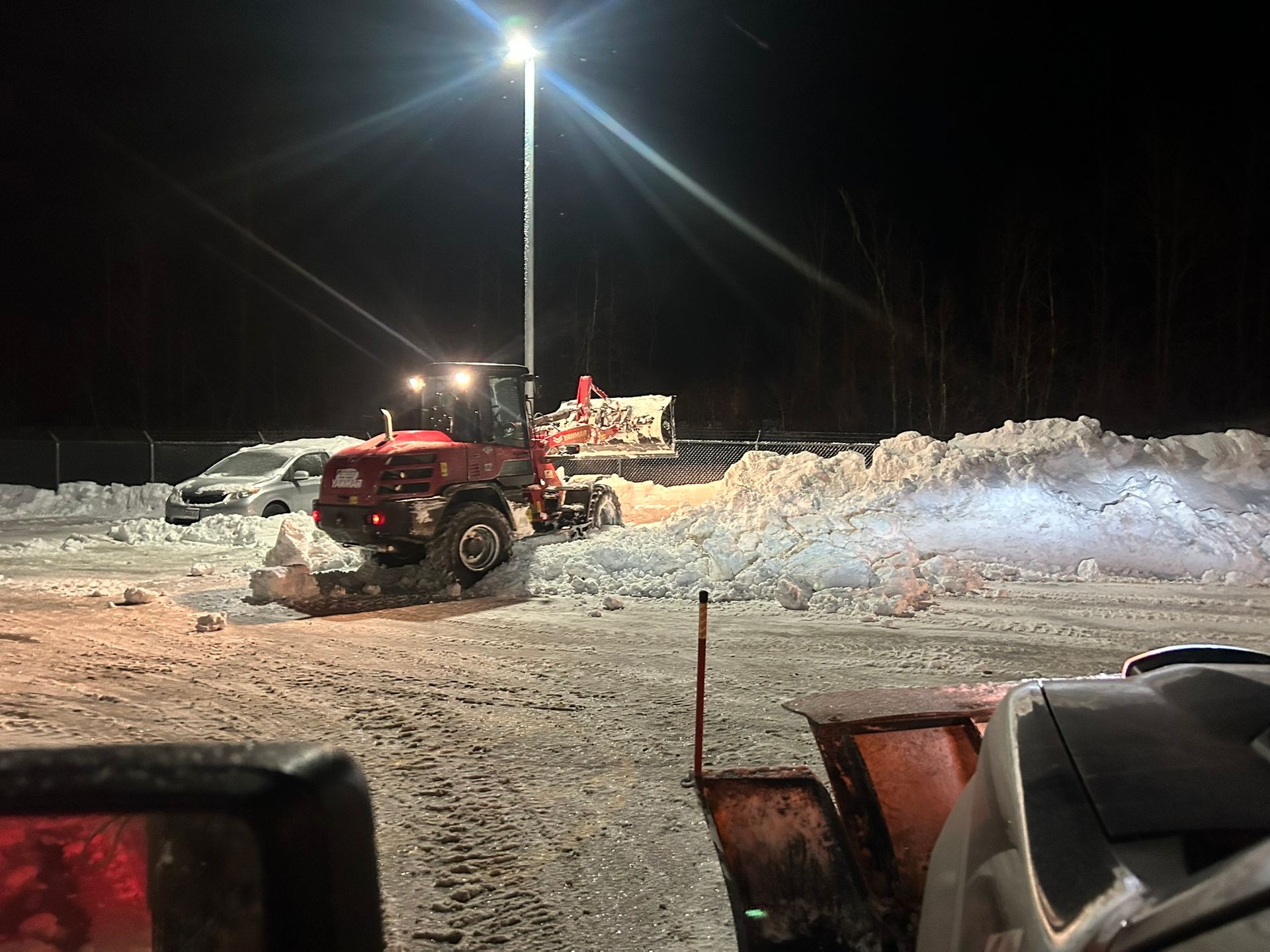 A red tractor is plowing snow in a parking lot at night.