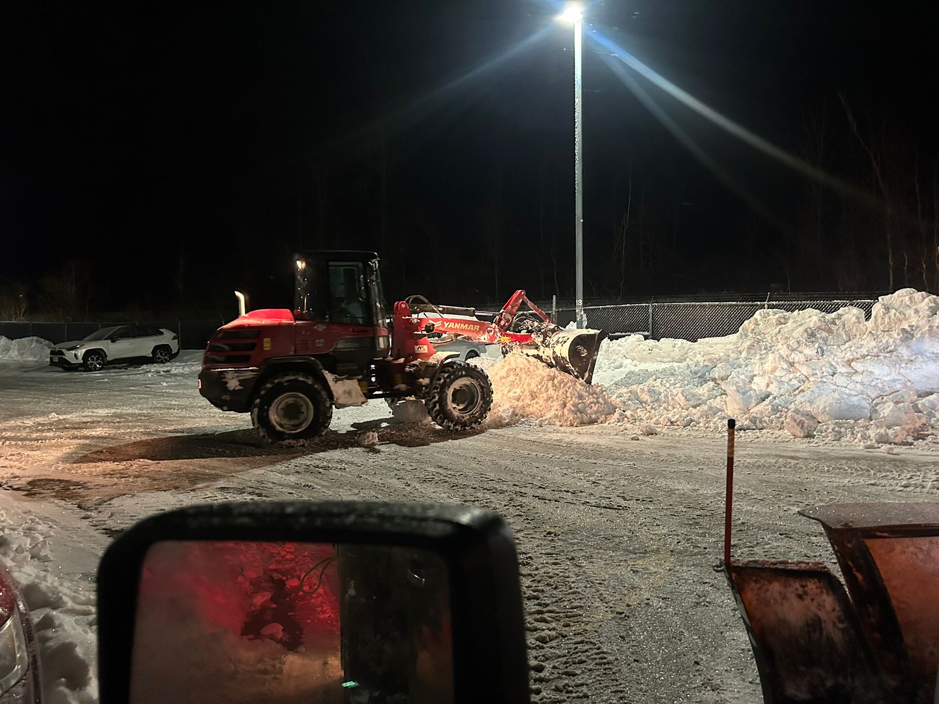 A snow plow is clearing snow from a parking lot at night.