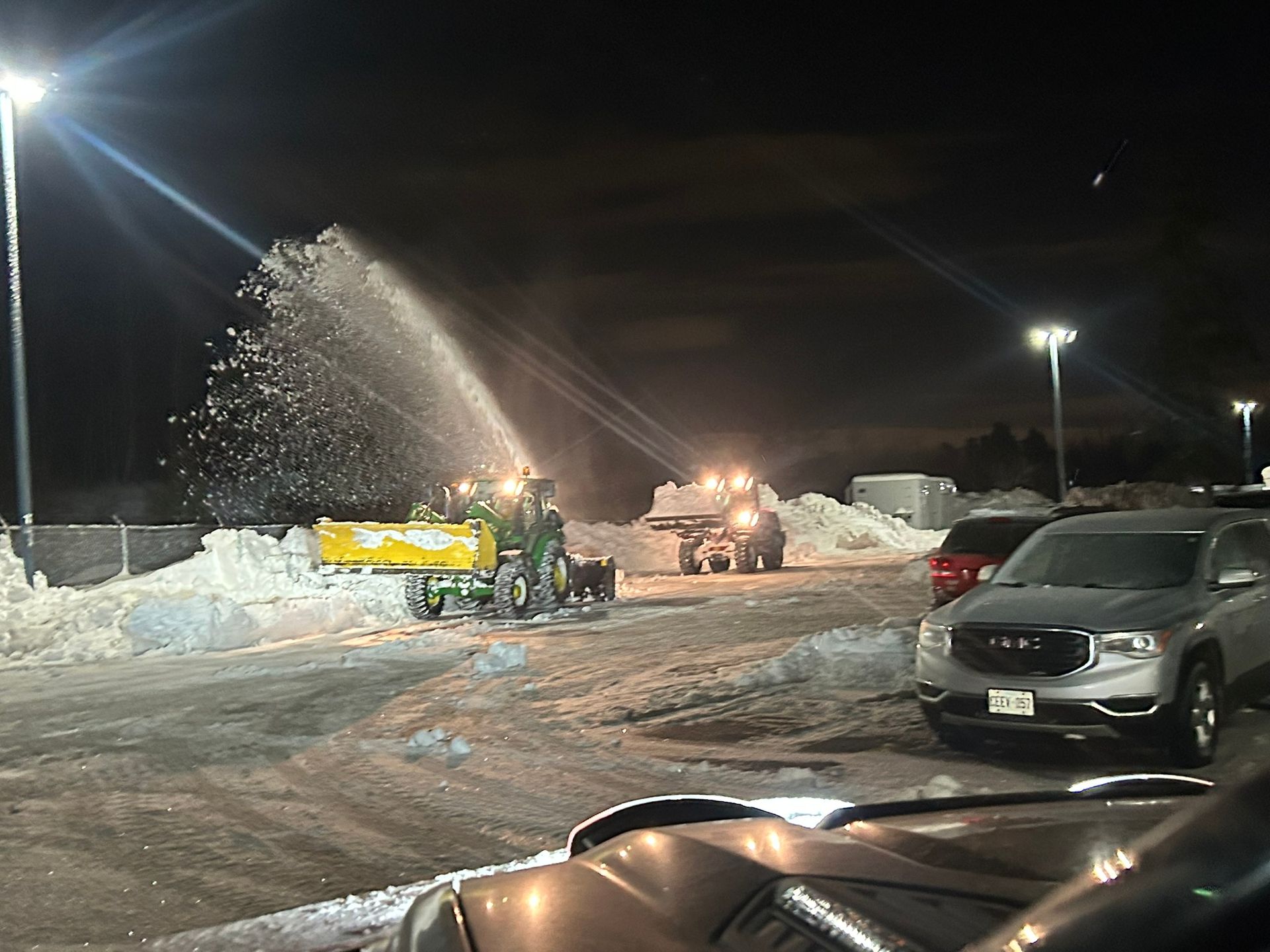 A snow blower is blowing snow in a parking lot at night
