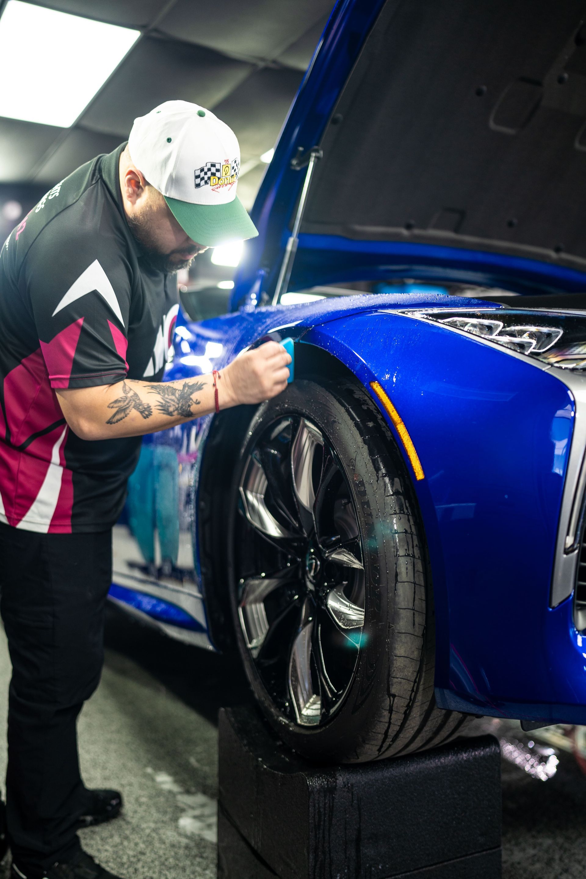 Mechanic inspecting the front wheel of a blue sports car with the hood open