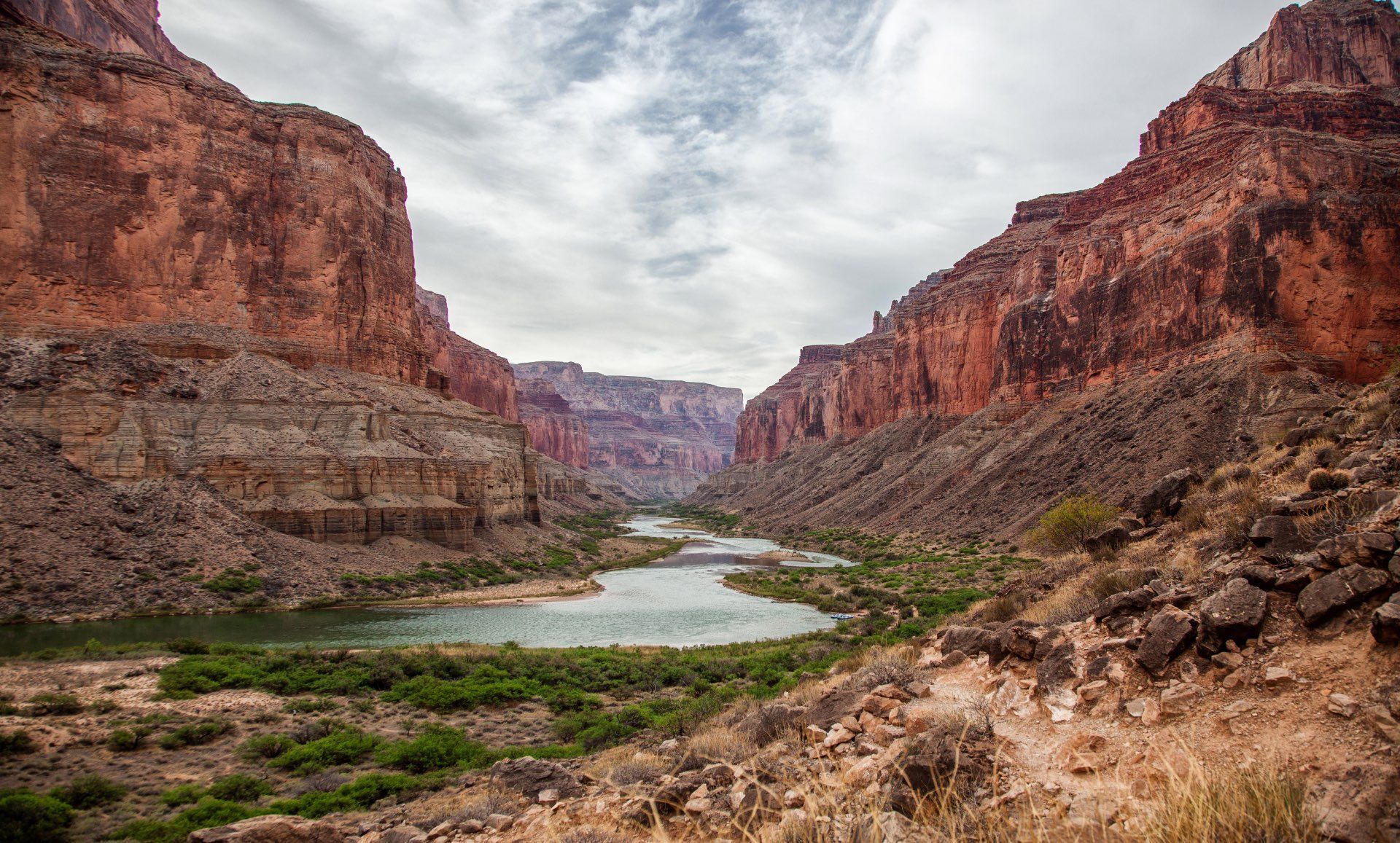 River winding through a canyon with red rock walls under a cloudy sky.