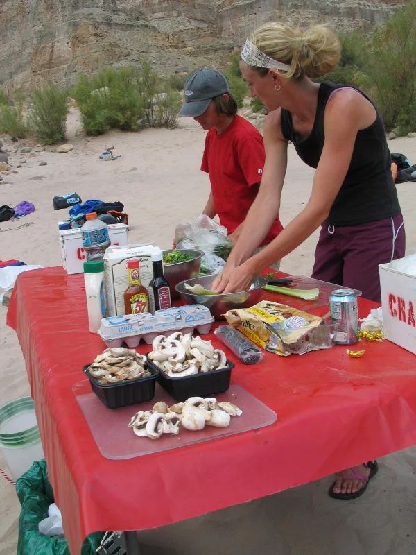 Two people preparing food on a red table outdoors. Mushrooms, eggs, and ingredients are visible.