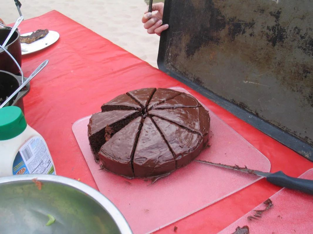 Chocolate cake sliced into wedges on a pink cutting board on a red table.
