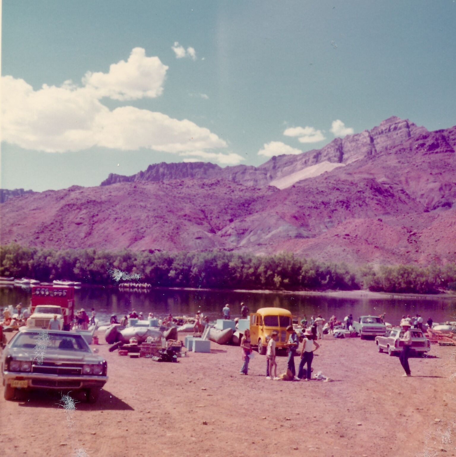 Beach scene with cars, yellow truck, people, and mountains in the background.