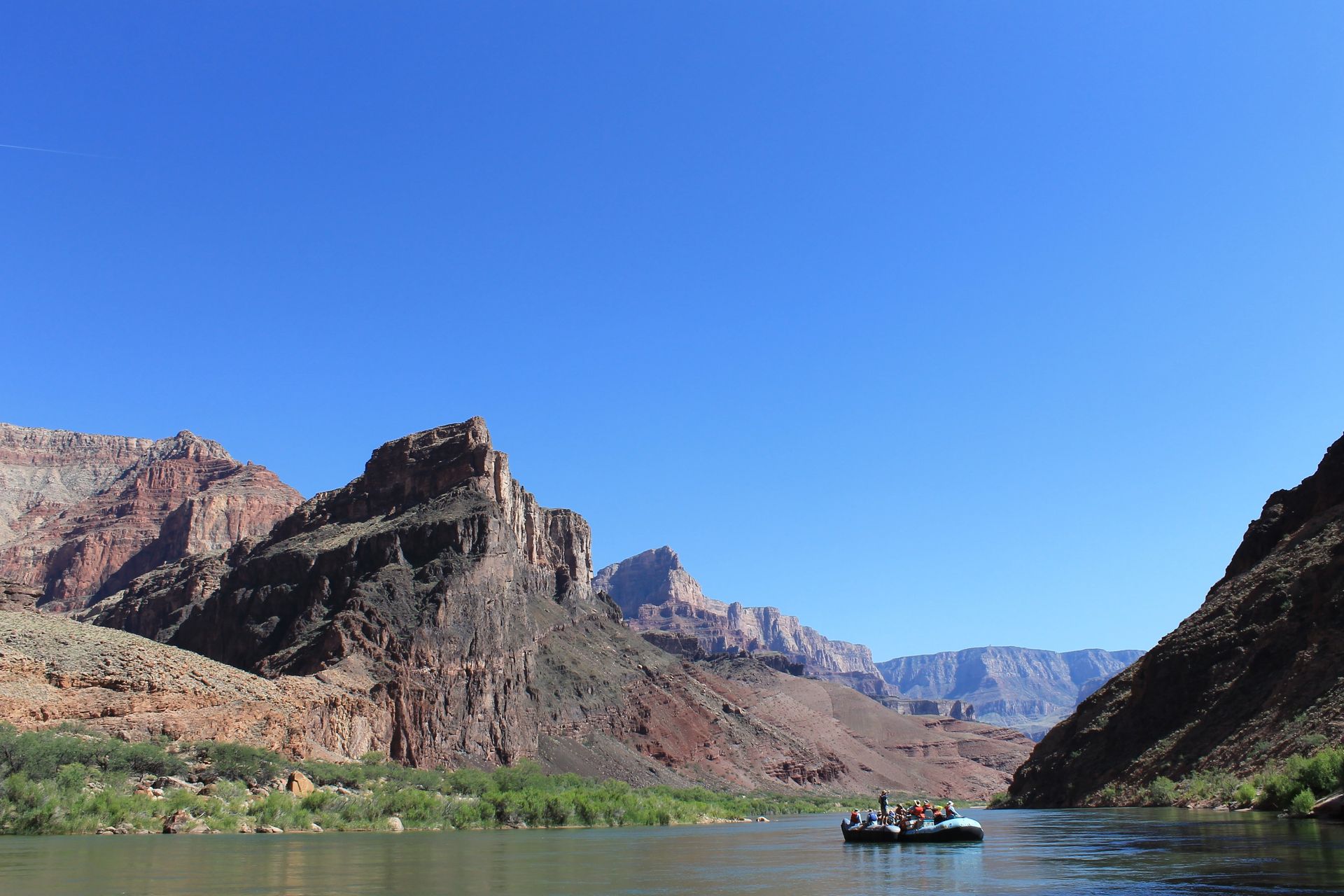 Raft on a river in a canyon, with towering red rock cliffs and a clear blue sky.