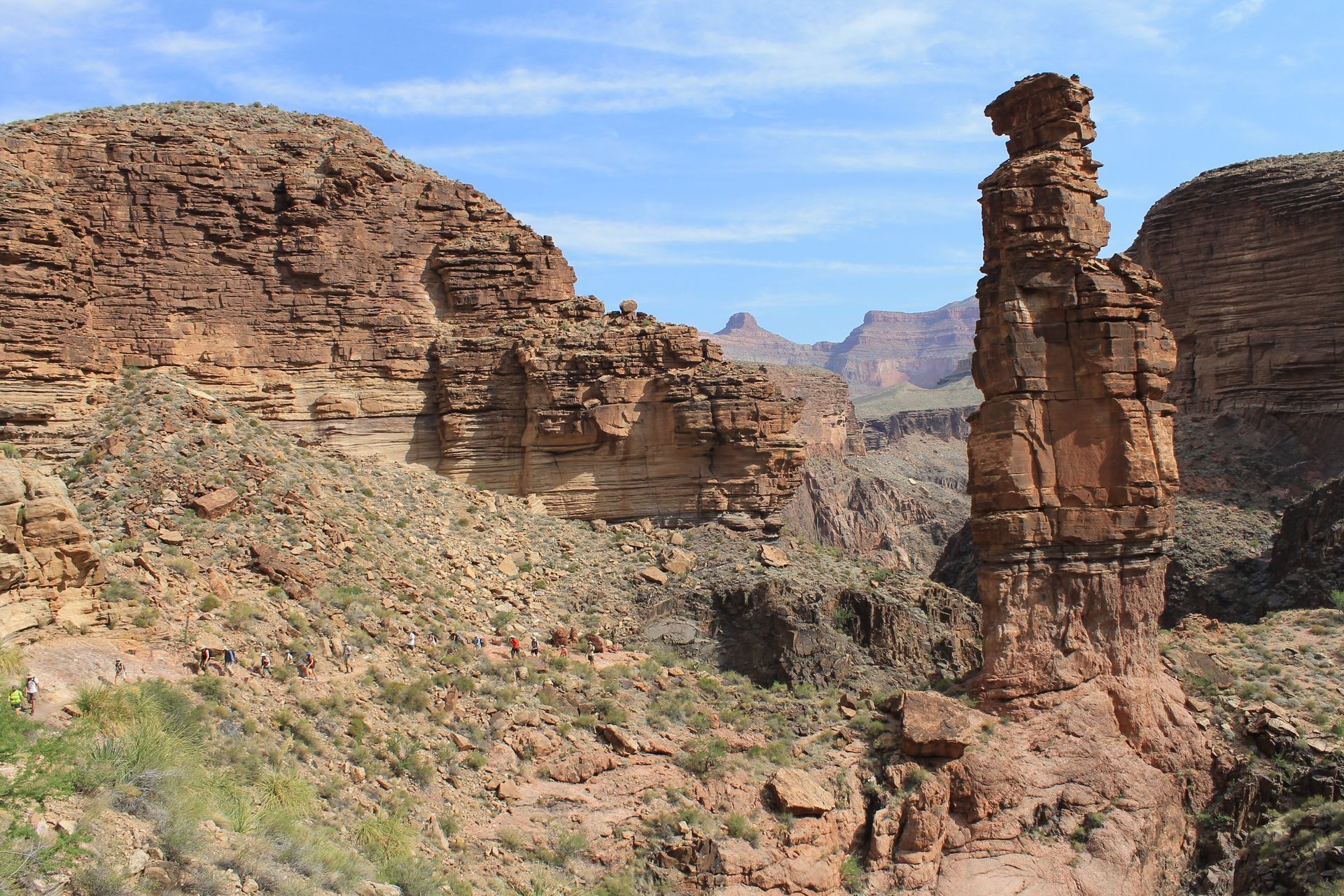 Canyon landscape with tall sandstone tower, rugged terrain, and blue sky.