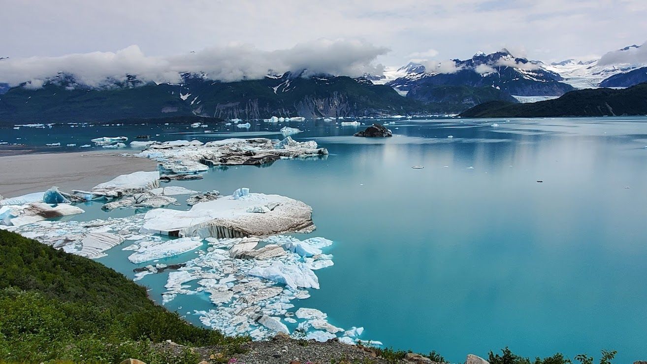 Turquoise glacier bay with floating icebergs and snowy mountains under a cloudy sky