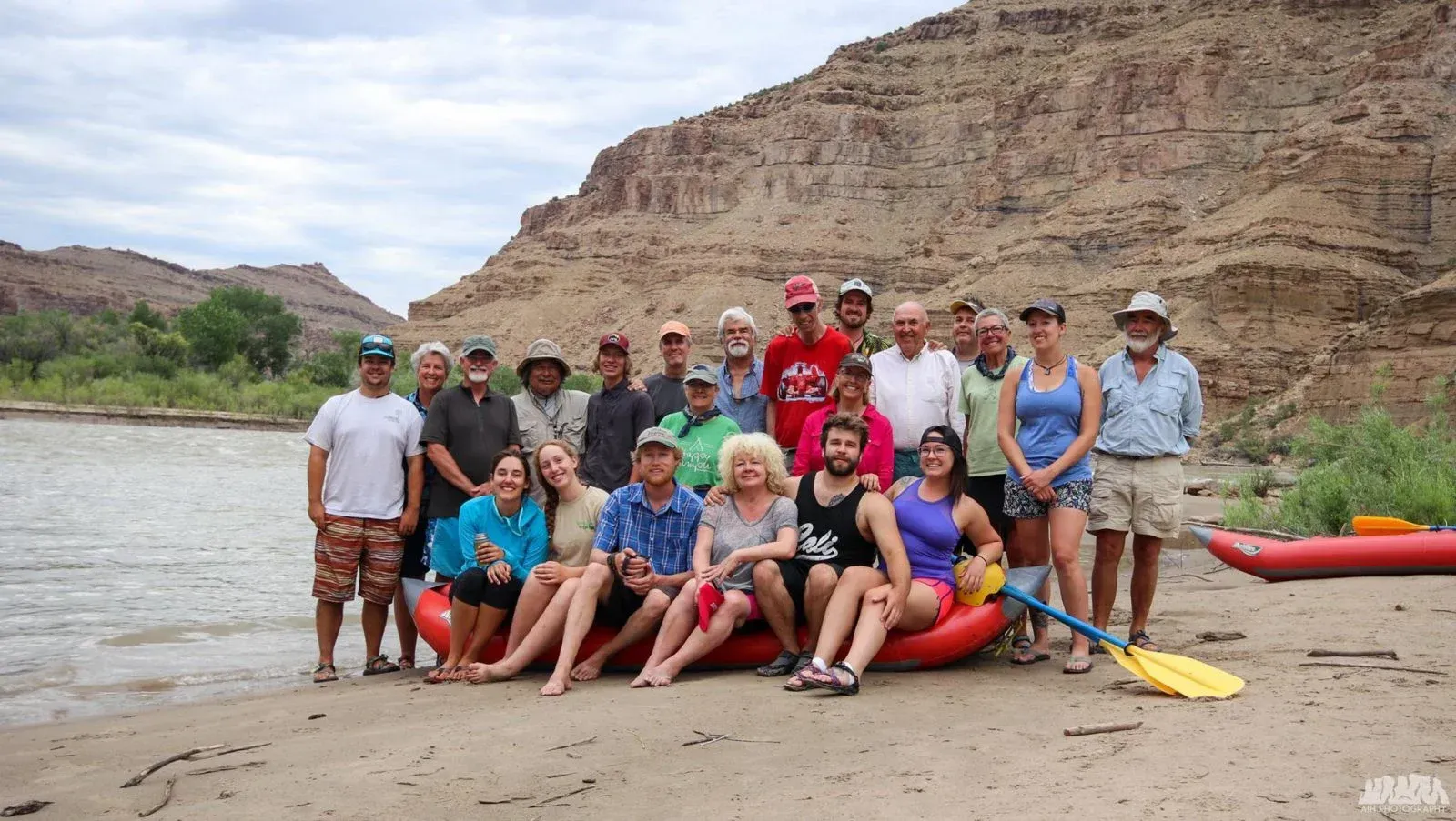 A very happy group of people sitting on an inflatable kayak with canyon walls in the background.
