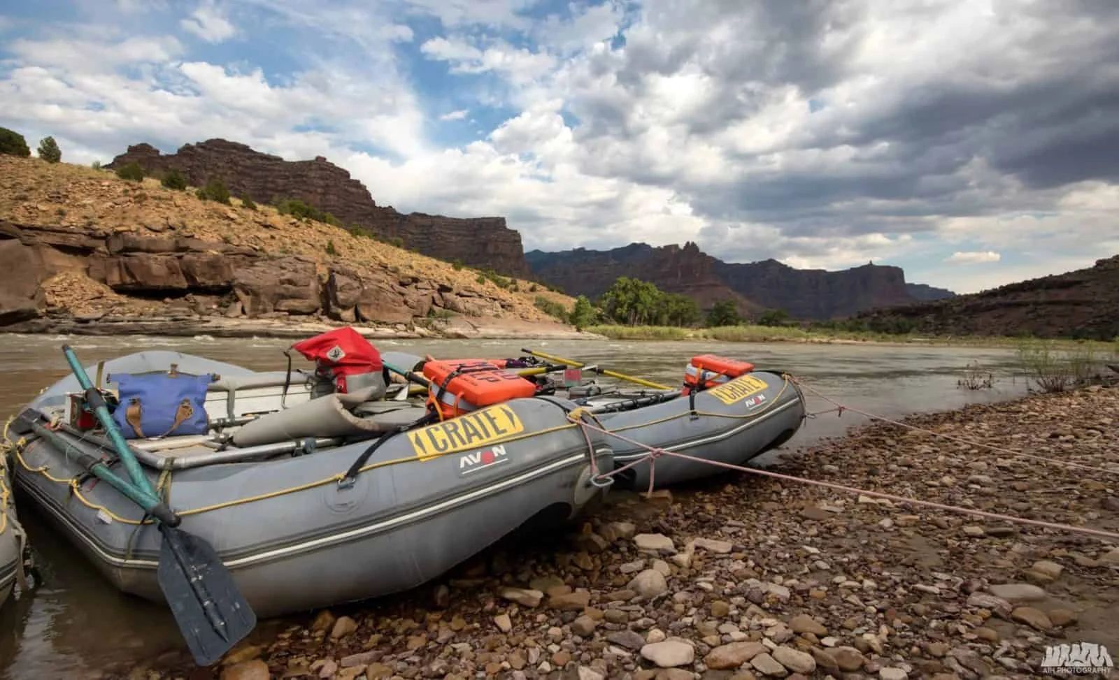 Two inflatable rafts on a rocky riverbank, brown canyon walls in the background under a cloudy sky.
