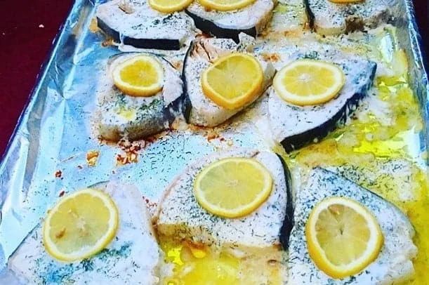 Baked fish slices with lemon on a foil-lined baking sheet.