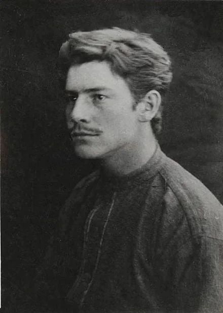 Man with mustache, dark hair, wearing a high-collared shirt, looking off-camera.