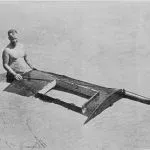 Man sitting on a long, thin, wooden structure extending into the water.
