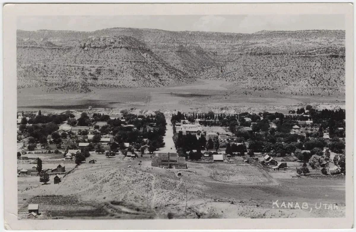 Panoramic view of Kanab, Utah, town nestled in a valley with mountains in the background. Black and white photograph.