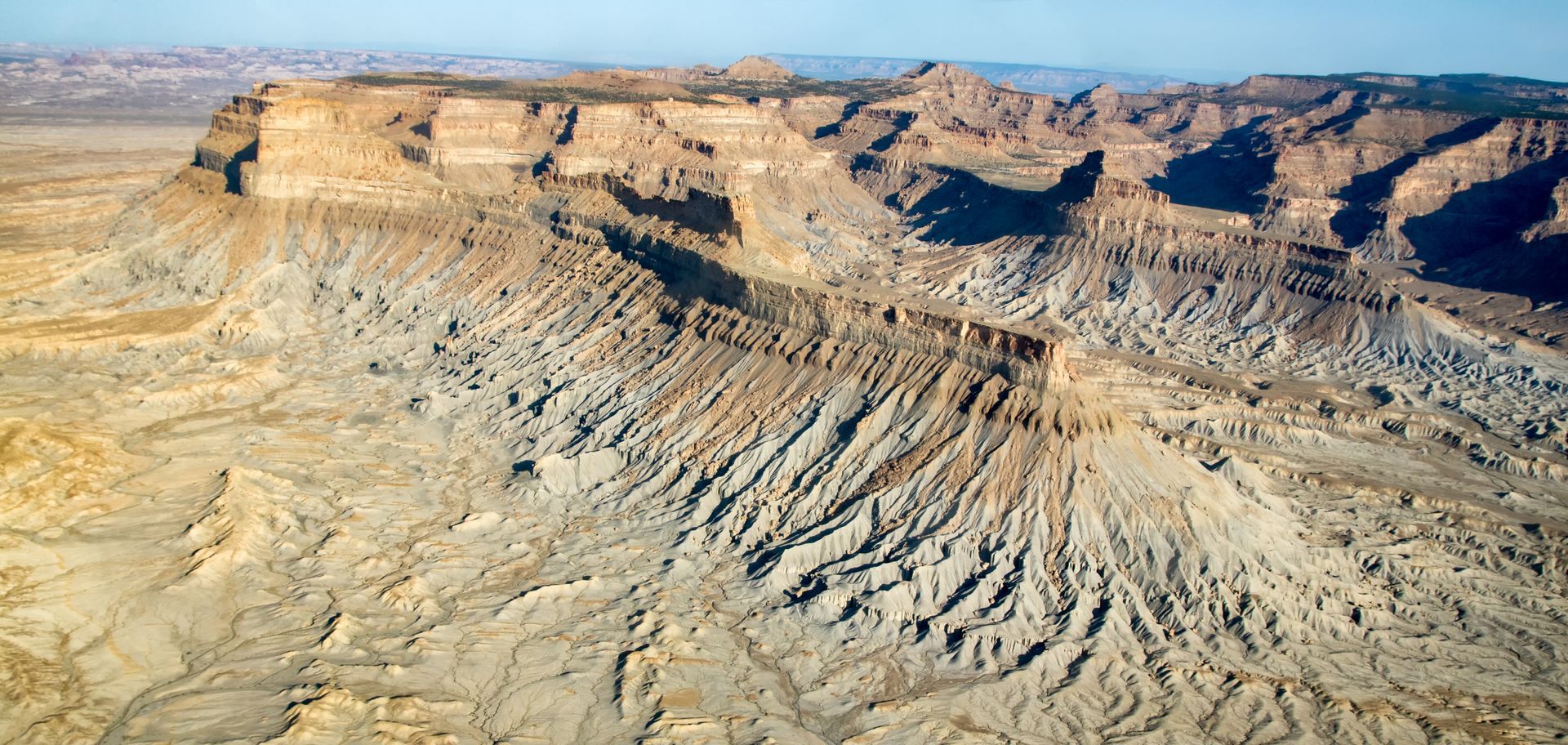 Aerial view of a rugged desert landscape with layered rock formations, in shades of brown and tan.