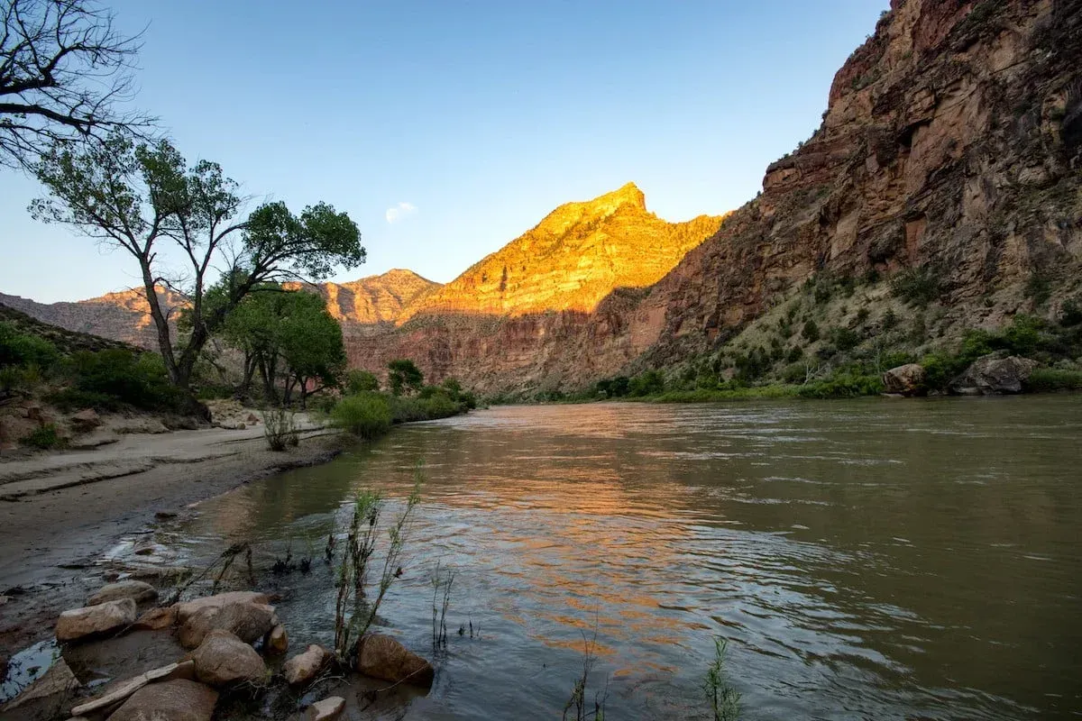 River flowing past mountains under a blue sky, with golden sunlight on the peaks.