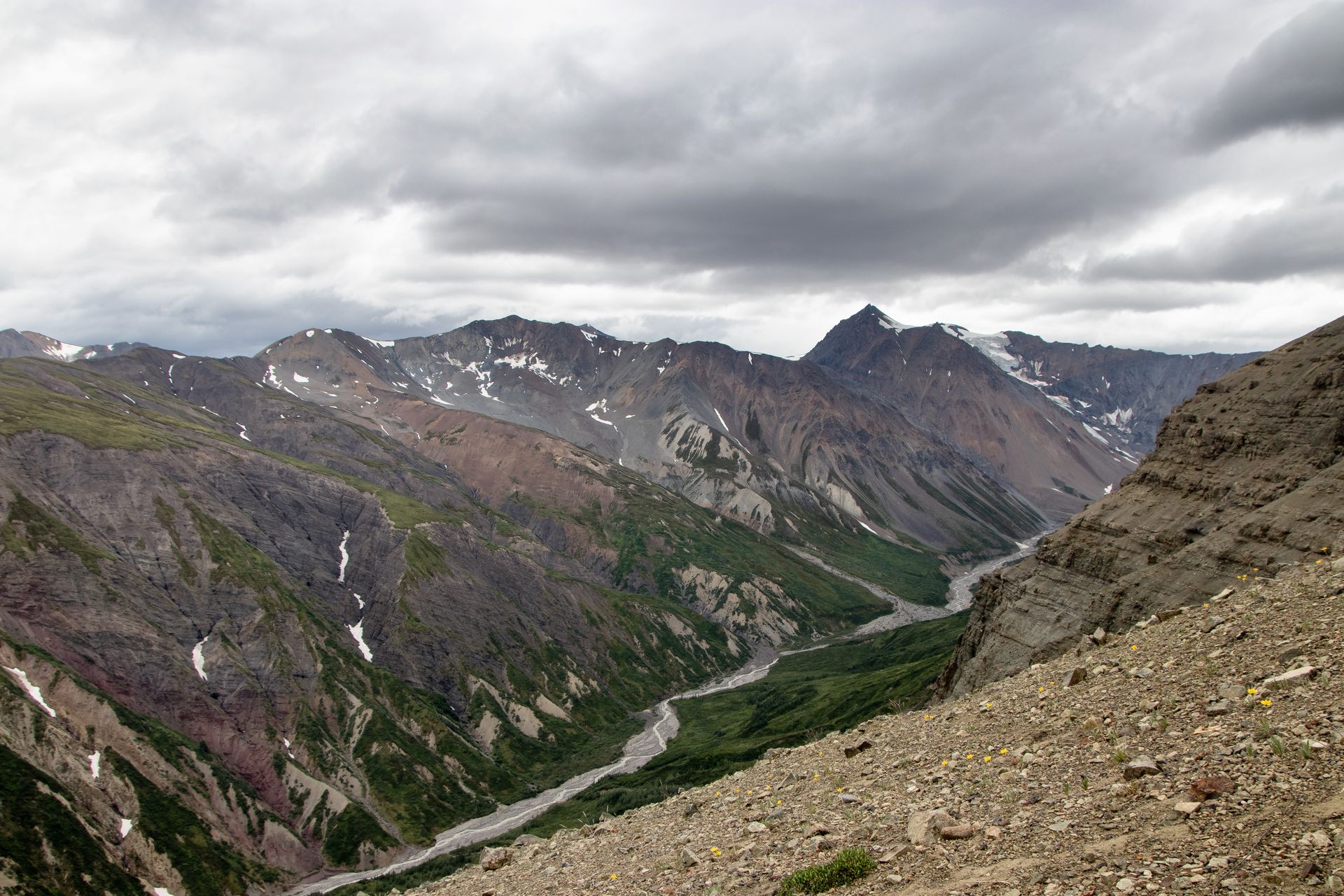 Mountain valley with a river winding through, under a cloudy sky.