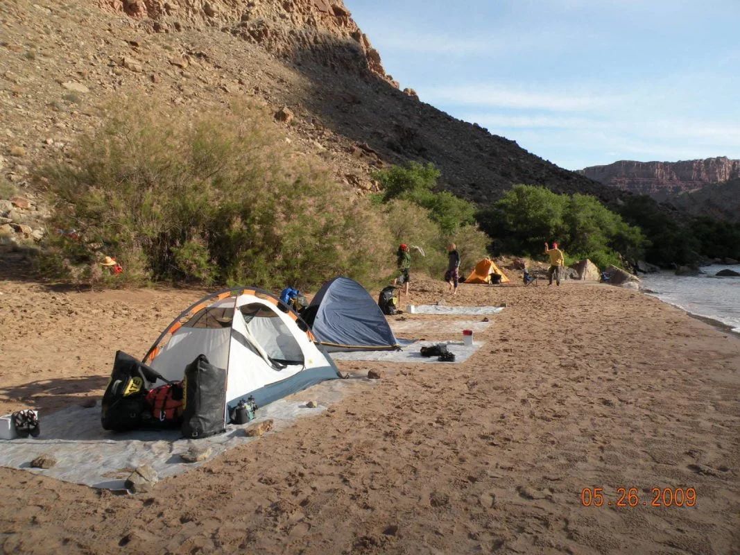 Camping tents on sandy beach at base of cliff; people near tents.