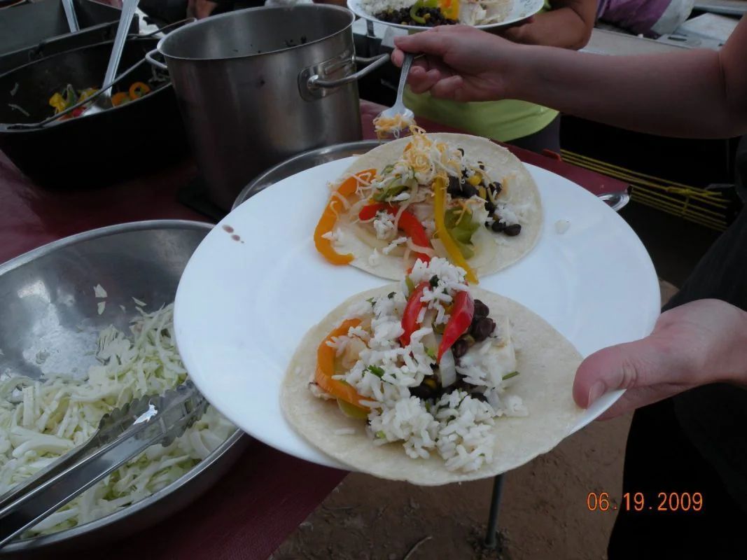 Person holding a plate with two tacos filled with rice, peppers, and beans. A bowl of slaw is nearby.