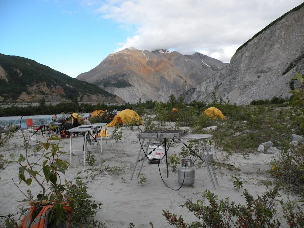 Camping scene with yellow tents, cooking area, and mountains.
