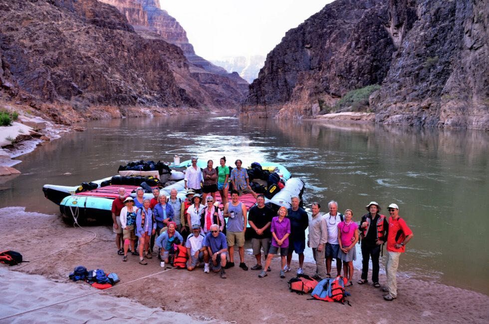 Group poses on a raft beside a river in a canyon.