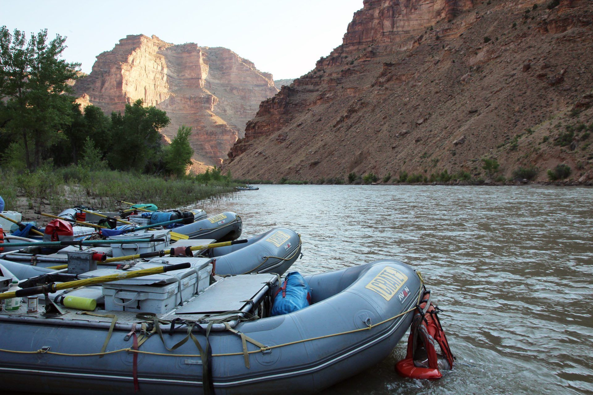 Rafts along a riverbank in a canyon with reddish-brown cliffs in the background.