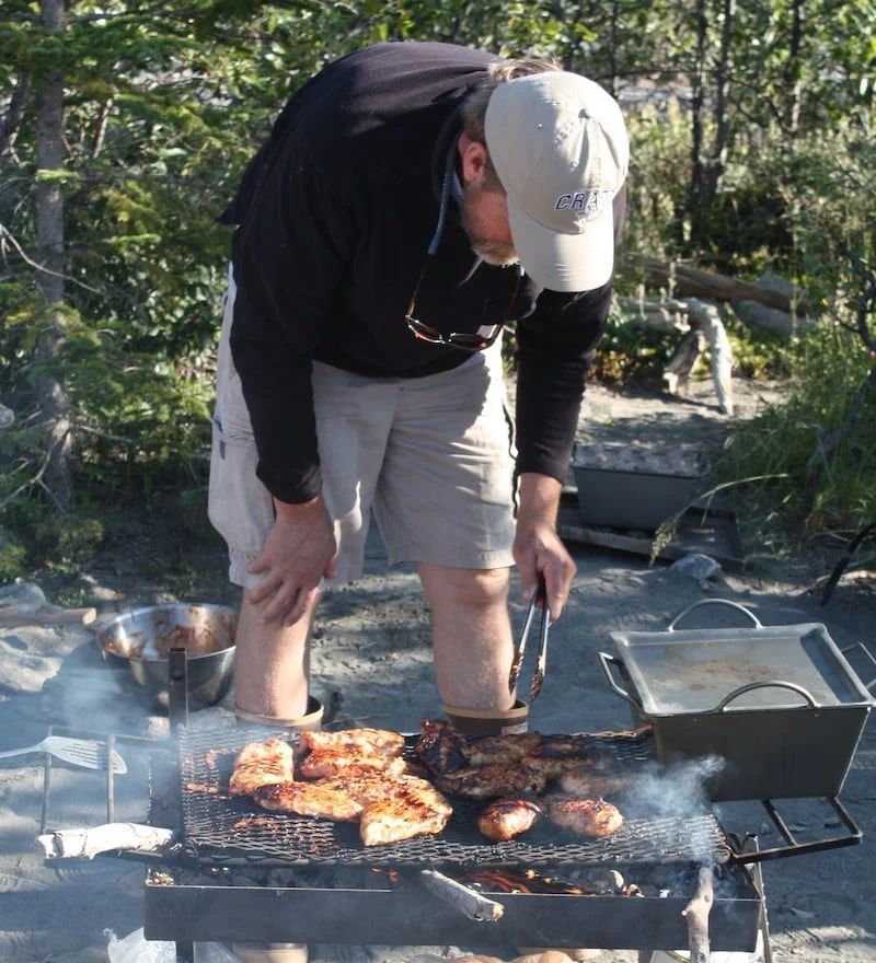 Person grilling meat outdoors, using tongs, with smoke rising.