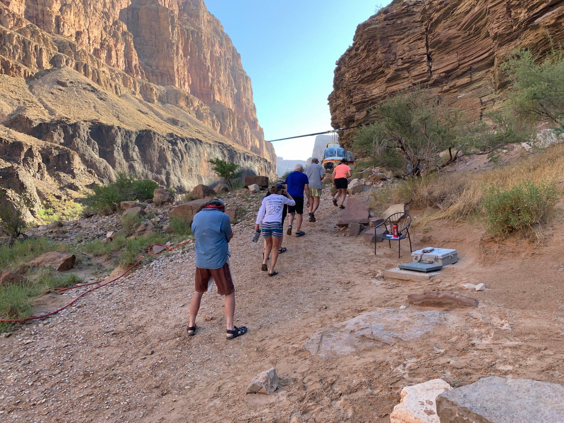People hiking uphill on a rocky path between canyon walls, sunny day.